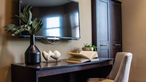 A flat-screen TV mounted on a wall, a dark wooden desk with a vase, a book, and a small plant. - Eton House (Yeovil)