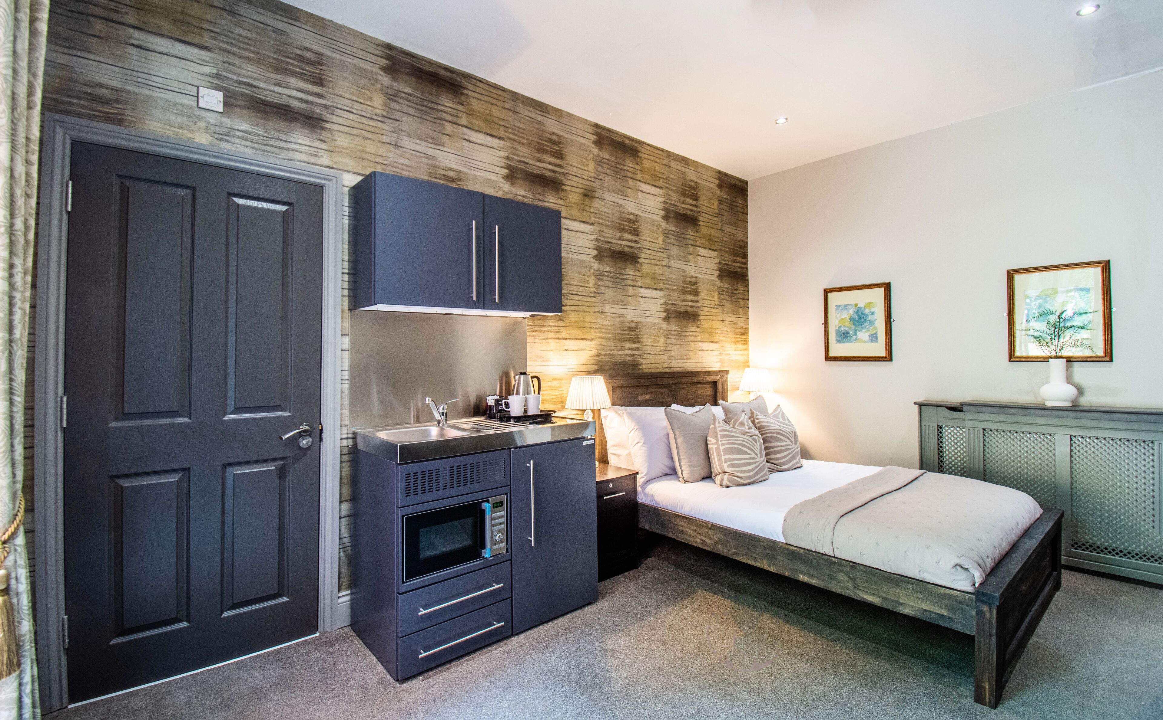 Un dormitorio compacto con cama, una kitchenette pequeña y una pared de acento de madera.