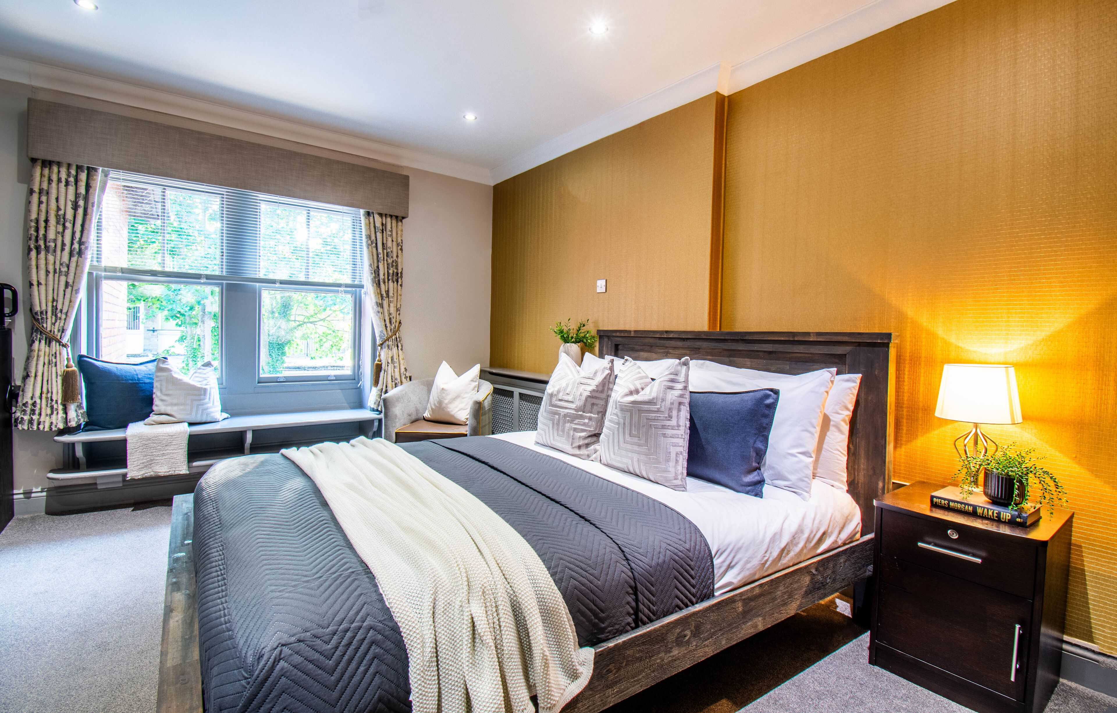 A bedroom with a large bed, a bedside table with a lamp, and a window with curtains.