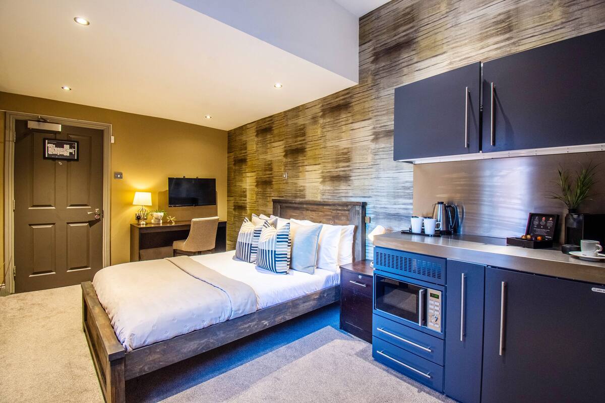 A modern hotel room with a large bed, a built-in desk, a flat-screen TV, a microwave, and a refrigerator.