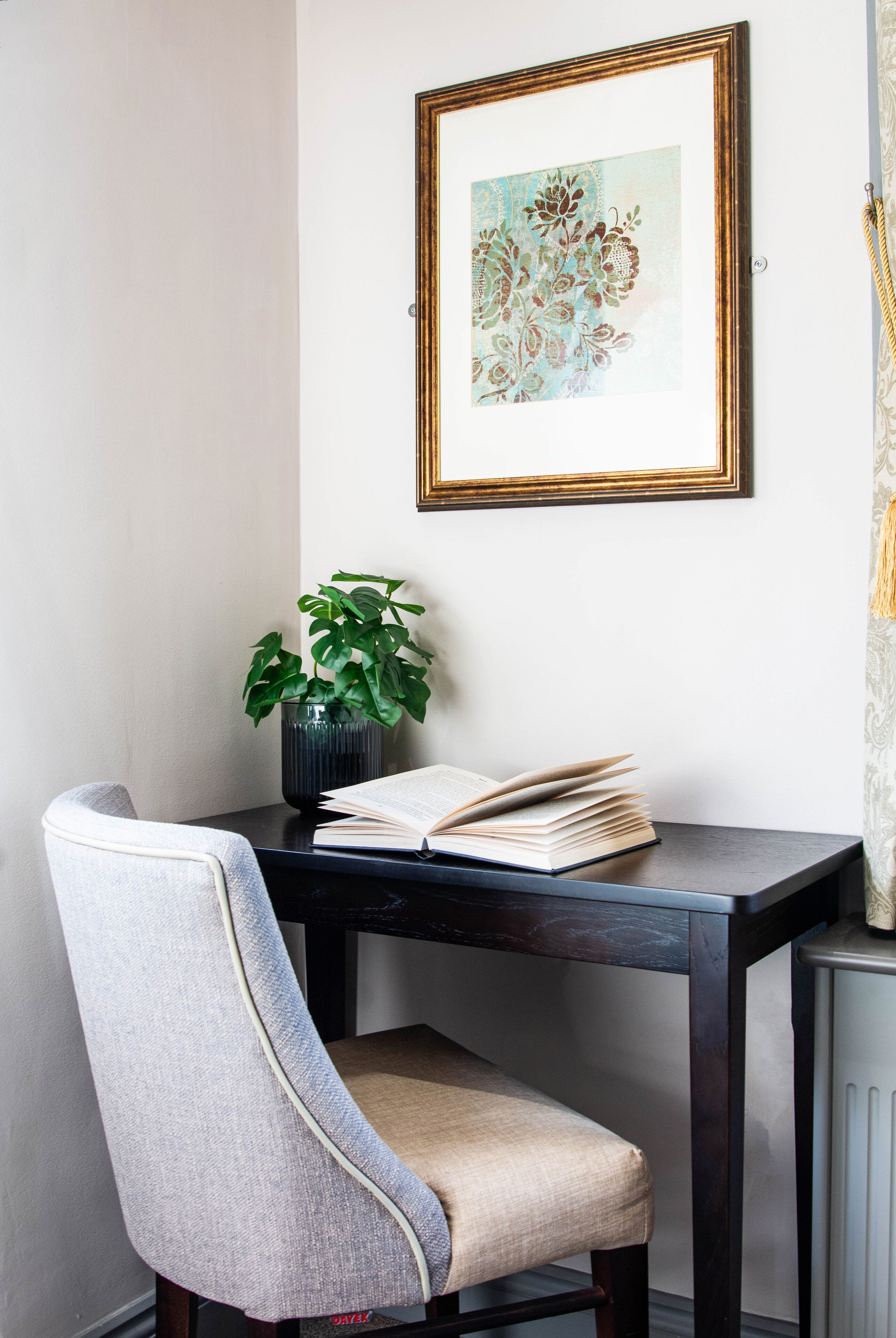 A corner room with a dark wooden table, a chair, a potted plant, and a framed artwork on the wall.