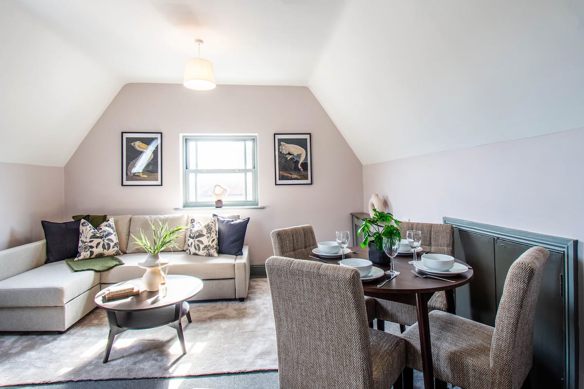 A cozy loft-style room with a dining area, a sofa, and a dining table set for two.