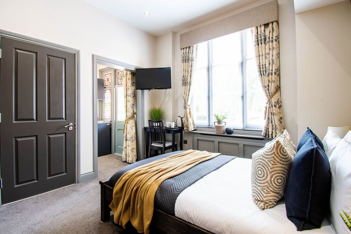 A hotel room with a bed, a desk with a chair, a TV, and a window with curtains.