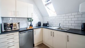 A kitchen with white cabinets, a dishwasher, a sink, and a window with a view. - Eton House (Yeovil)