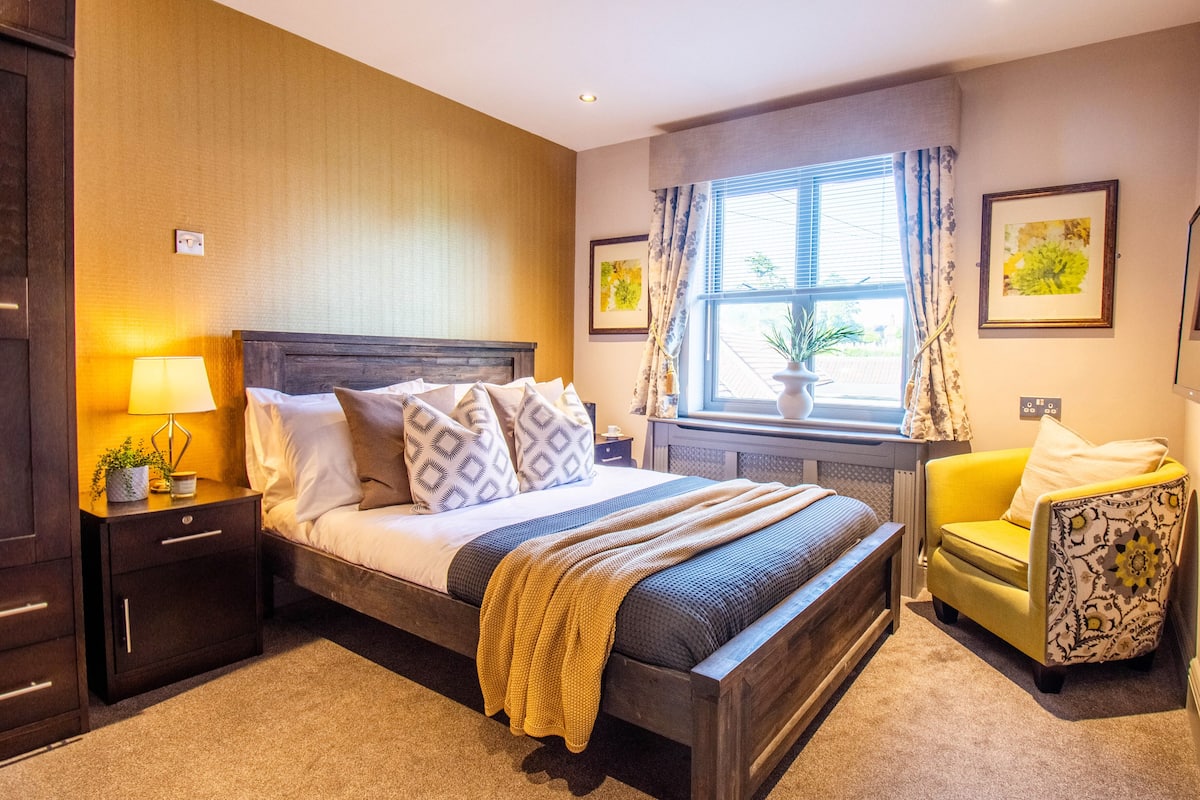 A neatly arranged bedroom with a bed, bedside table, lamp, and a window with curtains.