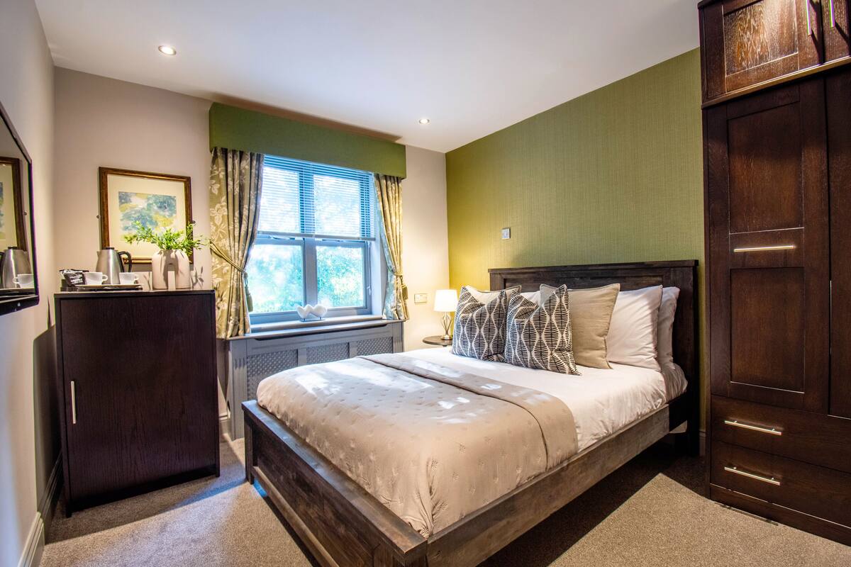 A bedroom with a large bed, a dresser, a window with curtains, and a radiator.