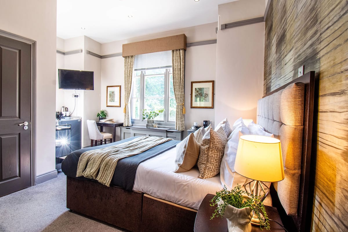 A bedroom with a bed, bedside table, lamp, and a desk with a chair.