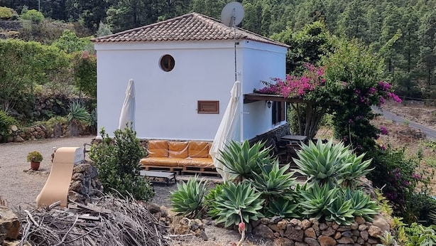 Un piccolo edificio bianco con tetto in tegole, un'antenna parabolica e una zona relax esterna coperta con cuscini.