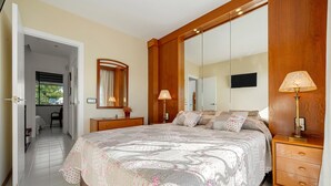 A bedroom with a large bed, a wooden nightstand, a bedside lamp, a mirror, and a television on the wall. - Holiday Home 'Ca La Montse' with Sea View, Private Terrace and Wi-Fi (Altafulla)