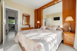 A bedroom with a large bed, a wooden nightstand, a bedside lamp, a mirror, and a television on the wall. - Holiday Home 'Ca La Montse' with Sea View, Private Terrace and Wi-Fi (Altafulla)