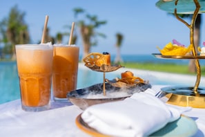 A table with two glasses of iced drinks, a decorative item, and a tray with food.