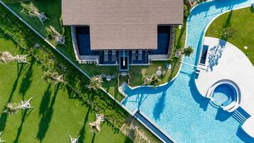 Vista aérea de un resort con piscina, un edificio grande de techo plano y céspedes cuidados.