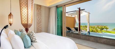 A bedroom with a large bed, a view of the ocean, and a balcony with lounge chairs.