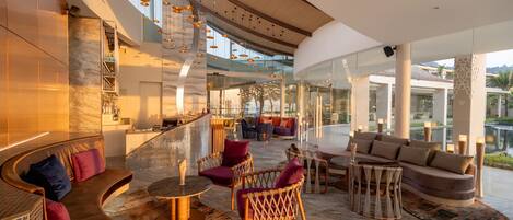 A spacious lobby with a curved sofa, wicker chairs, and a bar area.