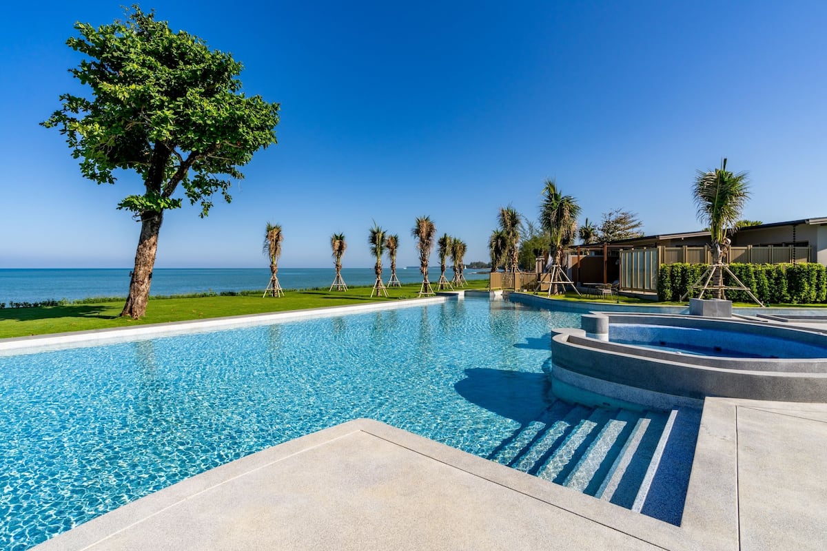 A swimming pool with clear blue water, surrounded by palm trees and a view of the ocean.