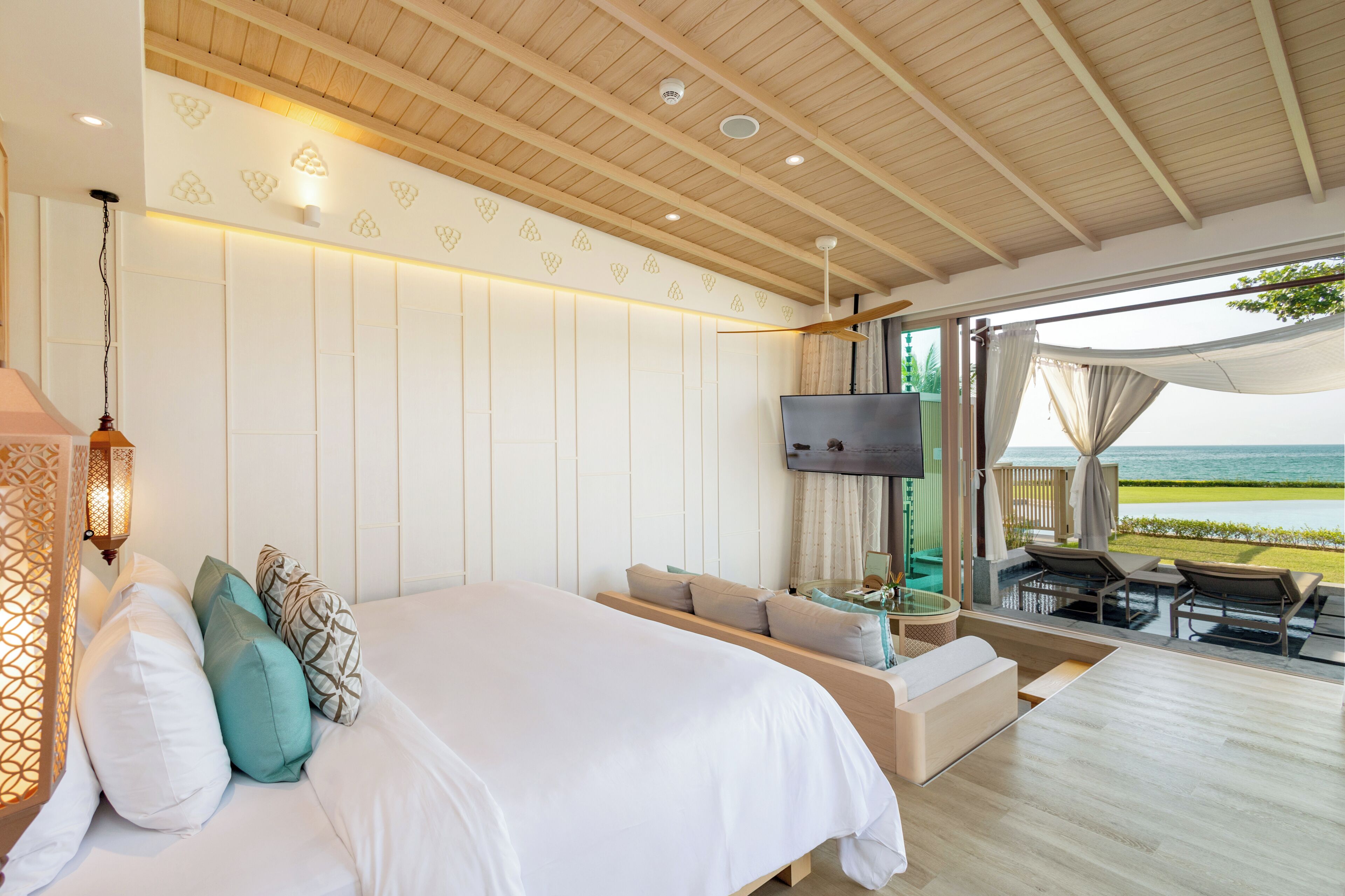 A bedroom with a bed, sofa, TV, and a balcony with a view of the sea.
