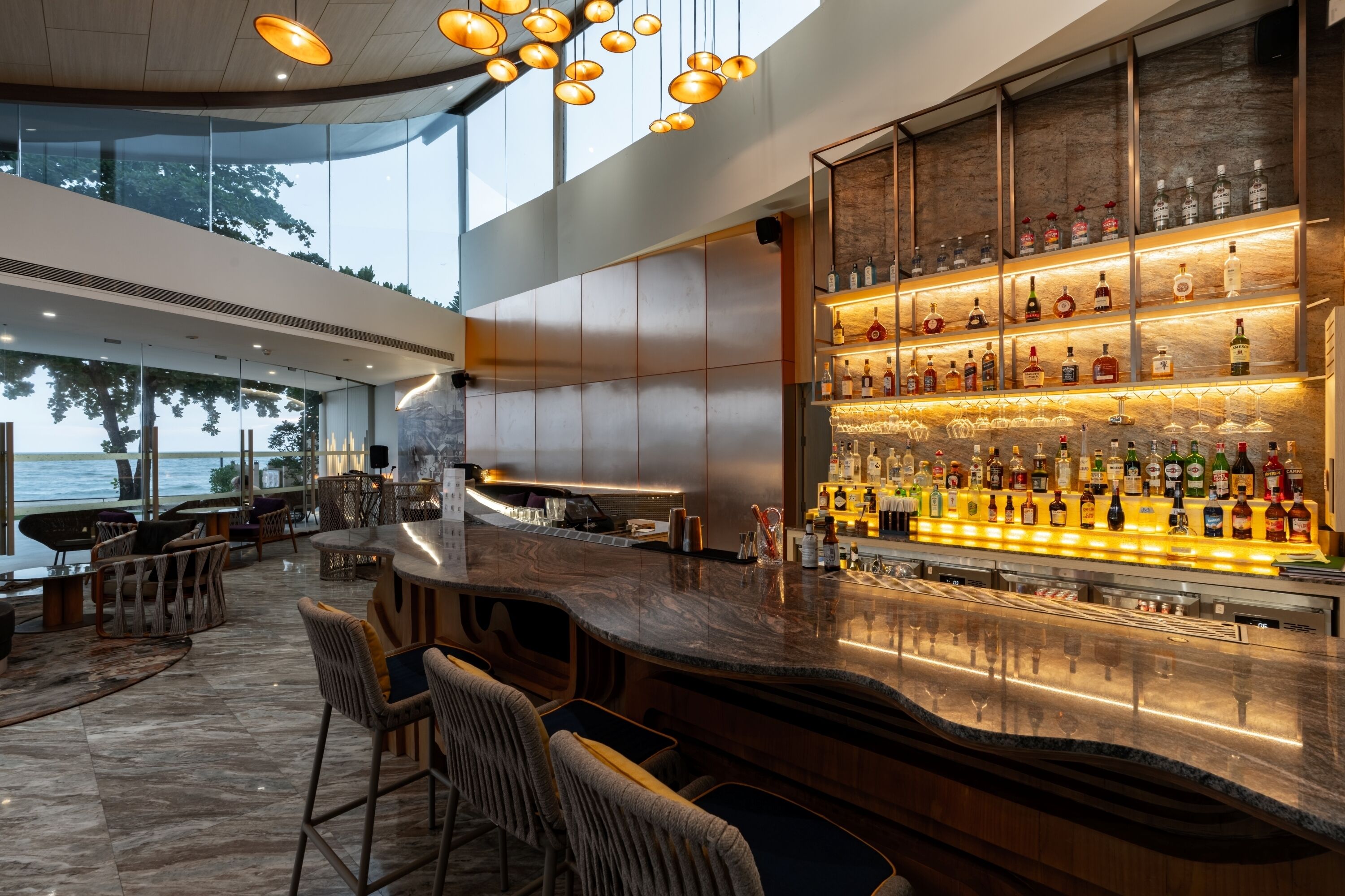 Un espace bar moderne doté d’un comptoir en marbre, de sièges et d’une variété de bouteilles d’alcool.