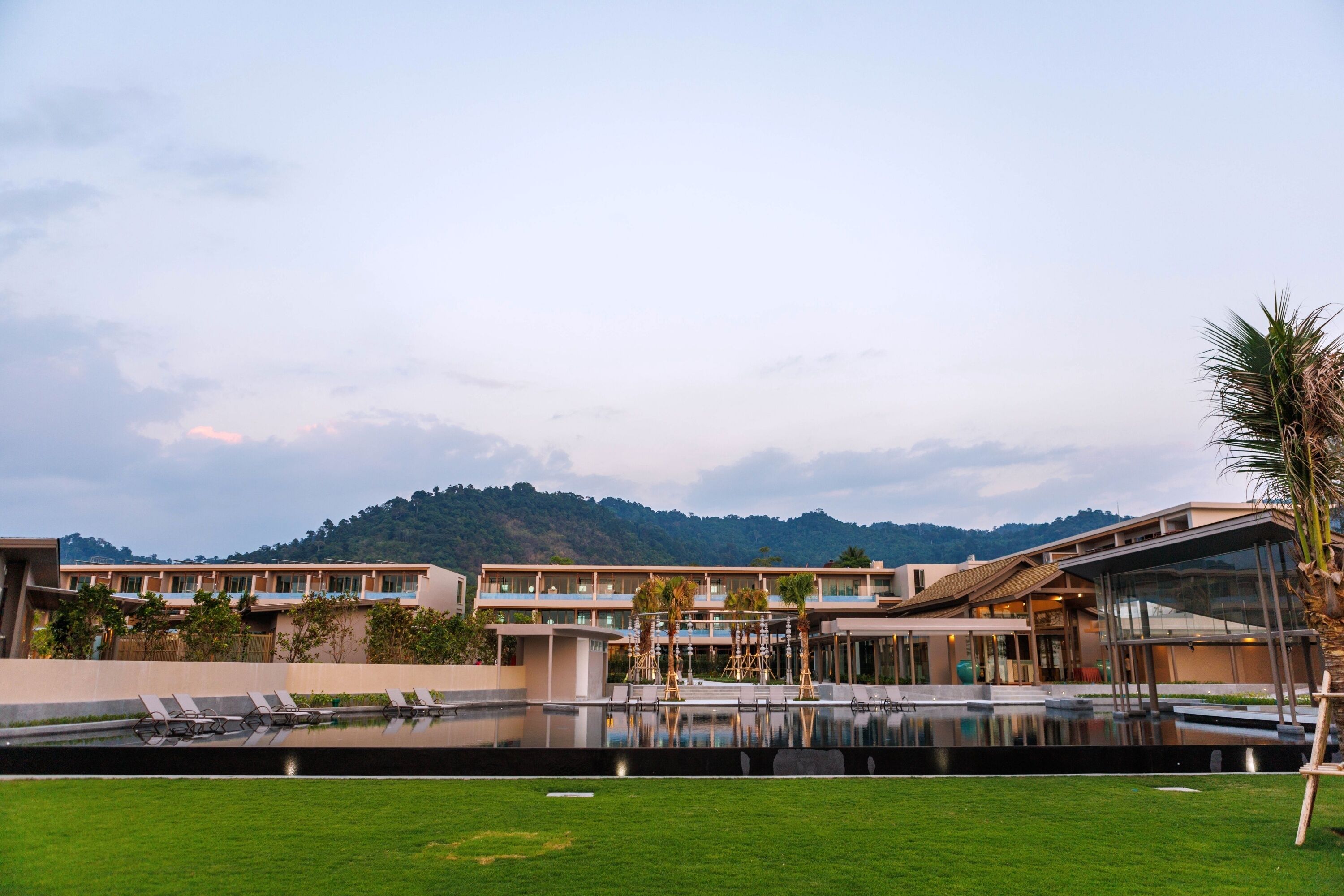 Un hotel moderno con piscina, sillas de descanso y vistas a una montaña.