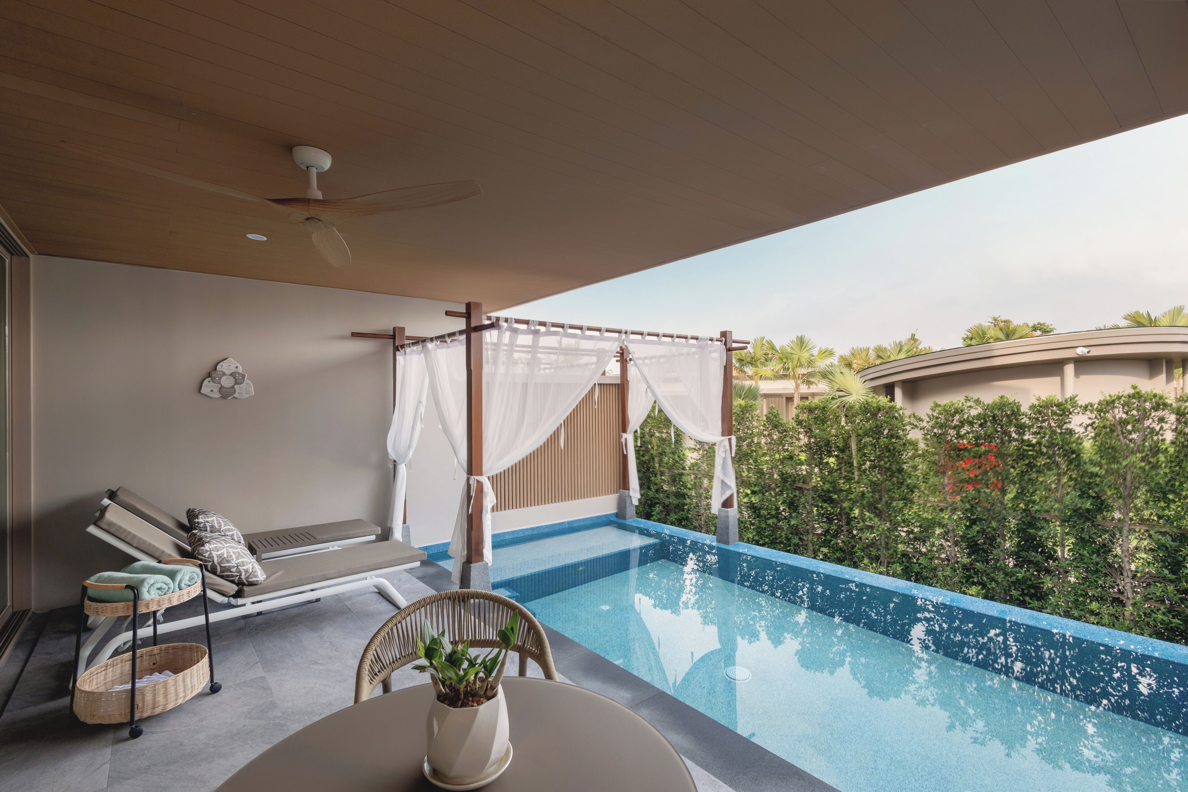 A poolside area with a lounge chair, a table with a potted plant, and a ceiling fan.