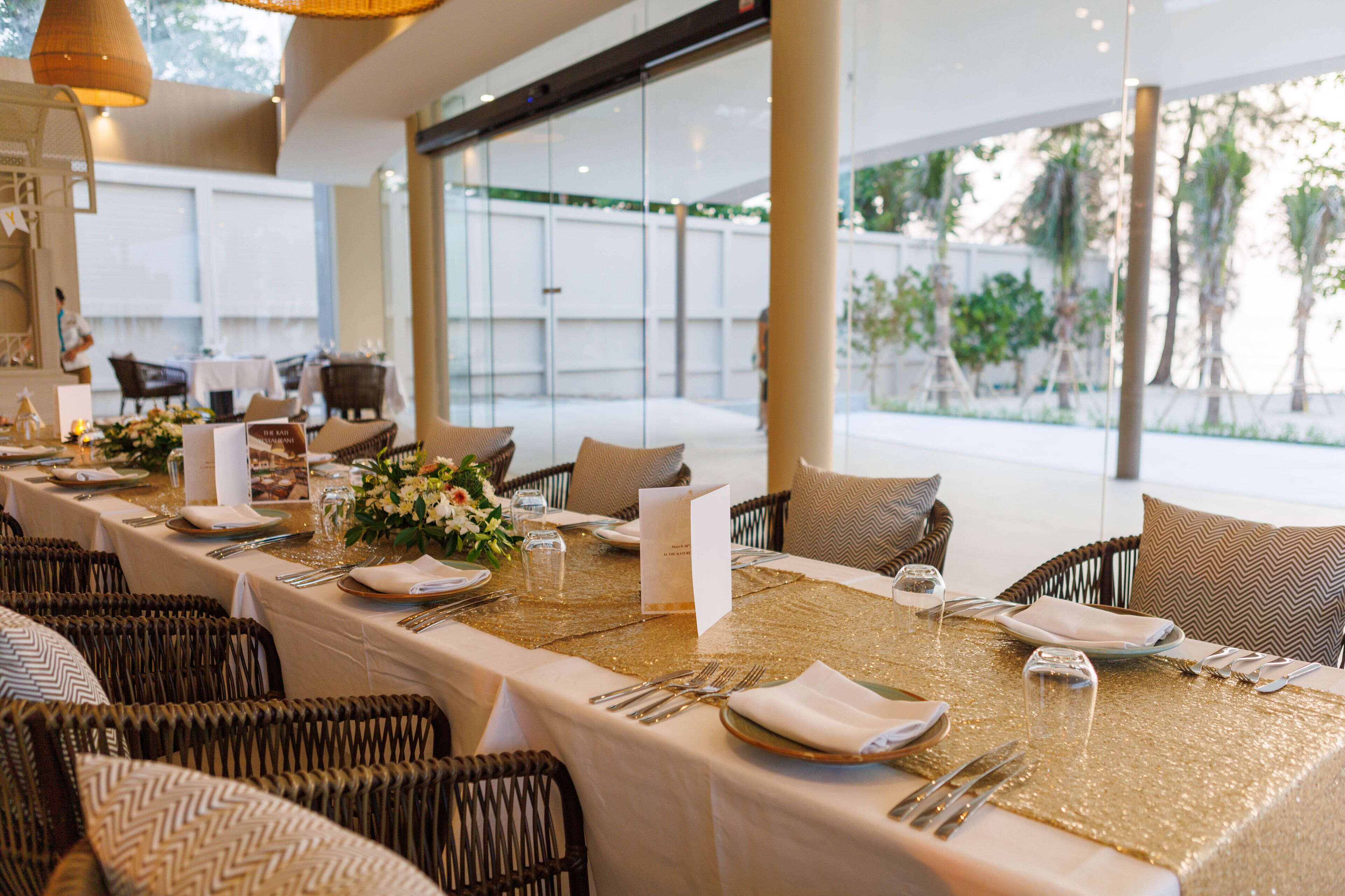 A dining area with a long table set for a meal, wicker chairs, and a view of the outdoors.