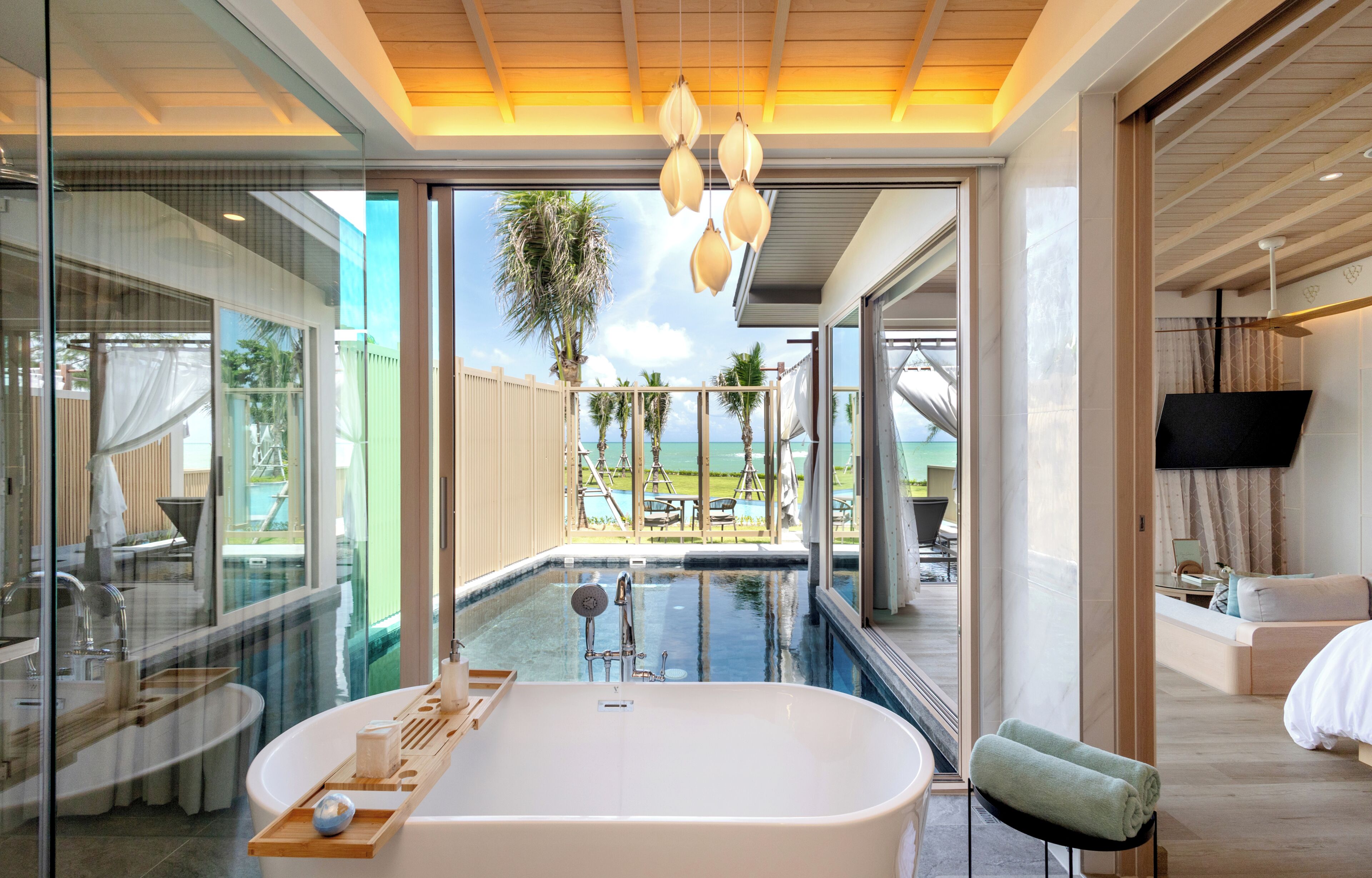 Un baño moderno con una bañera independiente, zona de ducha con mampara de cristal y vistas a una piscina y mobiliario exterior.