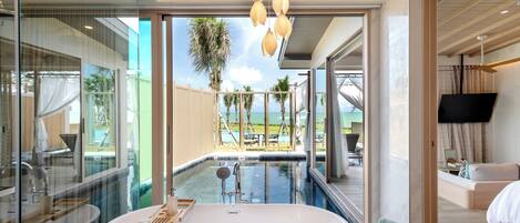 Un baño moderno con una bañera independiente, zona de ducha con mampara de cristal y vistas a una piscina y mobiliario exterior.