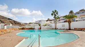 Une piscine avec des chaises longues, des palmiers et une chaîne de montagnes en arrière-plan.