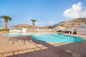 A swimming pool with a sun terrace, palm trees, and a mountainous backdrop. - Semi-Detached Bungalow 'La Casa De Ramón' with Sea View, Wi-Fi and Air Conditioning (Mogán)