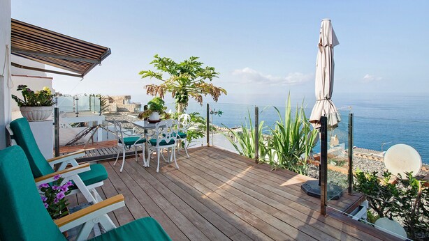 Une terrasse en bois avec des meubles d’extérieur, une table et une vue sur la mer.