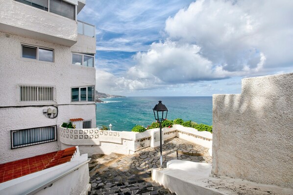 A coastal building with a stone-paved courtyard, a black street lamp, and a view of the sea.