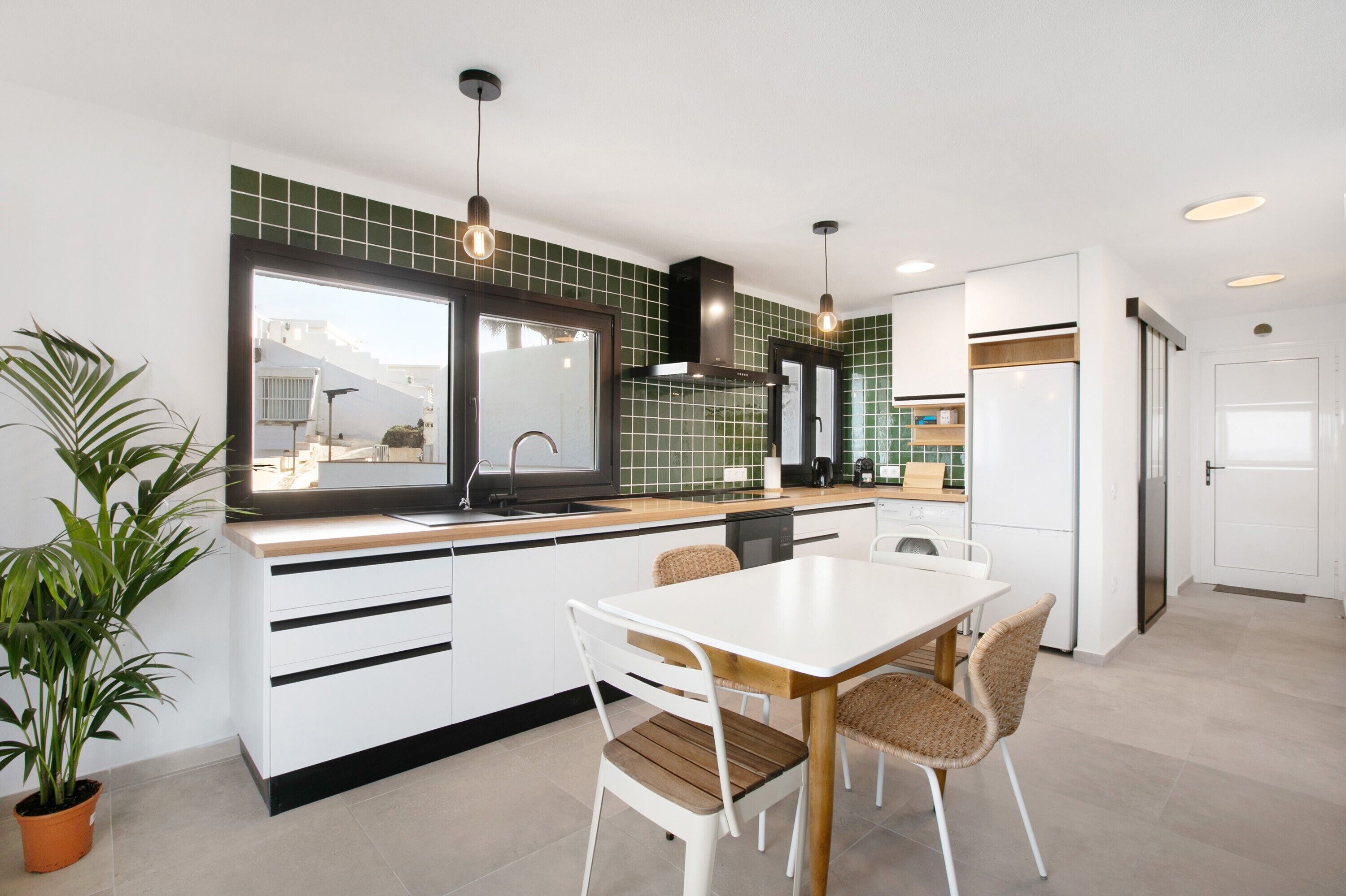 Una cocina moderna con armarios blancos, una mesa de comedor de madera y una planta en maceta.
