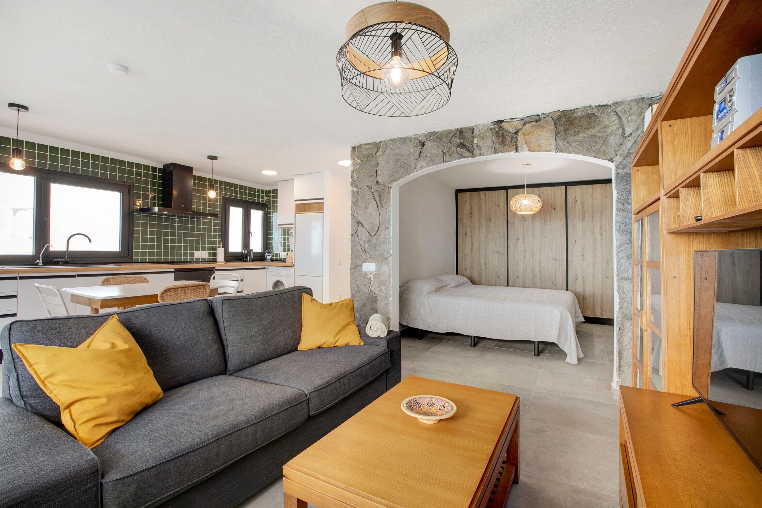 Un interior moderno con sofá, mesa de comedor, zona de cocina y dormitorio con cama.