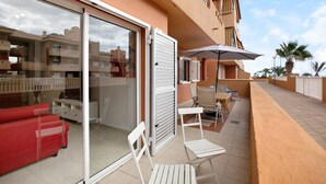 A hotel room with a sliding glass door, a red sofa, a white chair, and an outdoor umbrella. - Vacation Apartment 'Beach Front Puertito' with Shared Pool, Private Terrace and Wi-Fi (Güimar)