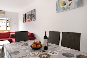 Zona pranzo con tavolo apparecchiato per due, una ciotola di frutta e una bottiglia di vino.