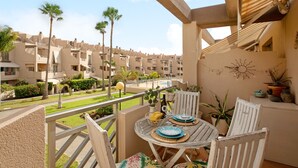 A balcony with a table set for two, overlooking a residential area with palm trees and a swimming pool. - Vacation Apartment 'La Casita De La Tejita' with Shared Pool and Wi-Fi (Granadilla)