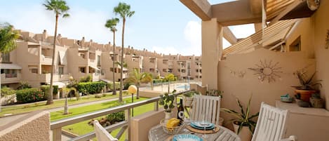 A balcony with a table set for two, overlooking a residential area with palm trees and a swimming pool.