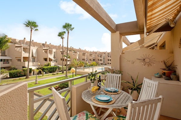 A balcony with a table set for two, overlooking a residential area with palm trees and a swimming pool.
