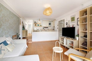 A living room with a sofa, a TV, and a dining area with a kitchen in the background.