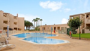 A swimming pool surrounded by lounge chairs, palm trees, and a building with balconies. - Vacation Apartment 'La Casita De La Tejita' with Shared Pool and Wi-Fi (Granadilla)