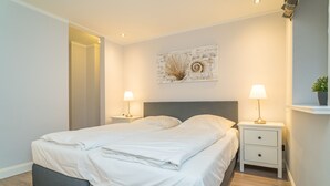 A modern bedroom with a large bed, two bedside tables, and a wall-mounted artwork. - Appartement Lachmöwe (Wenningstedt-Braderup (Sylt))