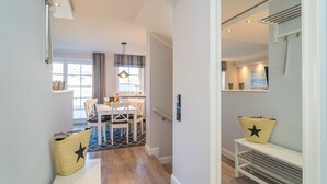 A modern interior with a dining area, a bench with a basket, and a hallway leading to a room with a shower. - Appartement Lachmöwe (Wenningstedt-Braderup (Sylt))