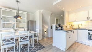 A modern kitchen with white cabinetry, a central island, and a dining area with white chairs and a table. - Appartement Lachmöwe (Wenningstedt-Braderup (Sylt))