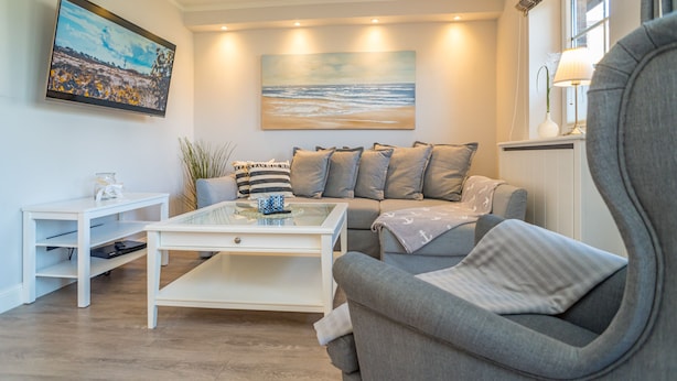 A living room with a sofa, coffee table, and a painting of a beach scene. - Appartement Lachmöwe (Wenningstedt-Braderup (Sylt))