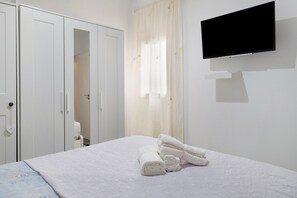 Een slaapkamer met een bed, een aan de muur bevestigde televisie en een kledingkast.
