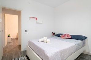 Une chambre à coucher avec un lit, une table de chevet, une petite plante et une porte donnant sur une autre pièce.