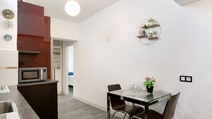 Una cocina moderna con microondas, una mesa de comedor de cristal y sillas. Se observa un armario marrón oscuro y una pared blanca con un estante circular.