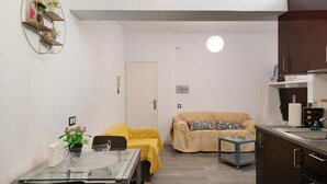 Un espacio habitable compacto con comedor, sofá, kitchenette y una puerta que da a otra habitación.