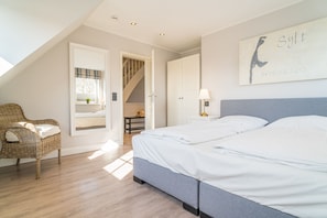 Quarto com uma cama grande, uma cadeira de vime, uma escada e uma obra de arte na parede.