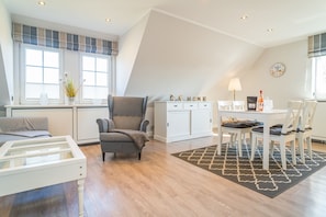 Uma sala de estar moderna com sofá, poltrona, mesa de jantar e uma grande janela com persianas.