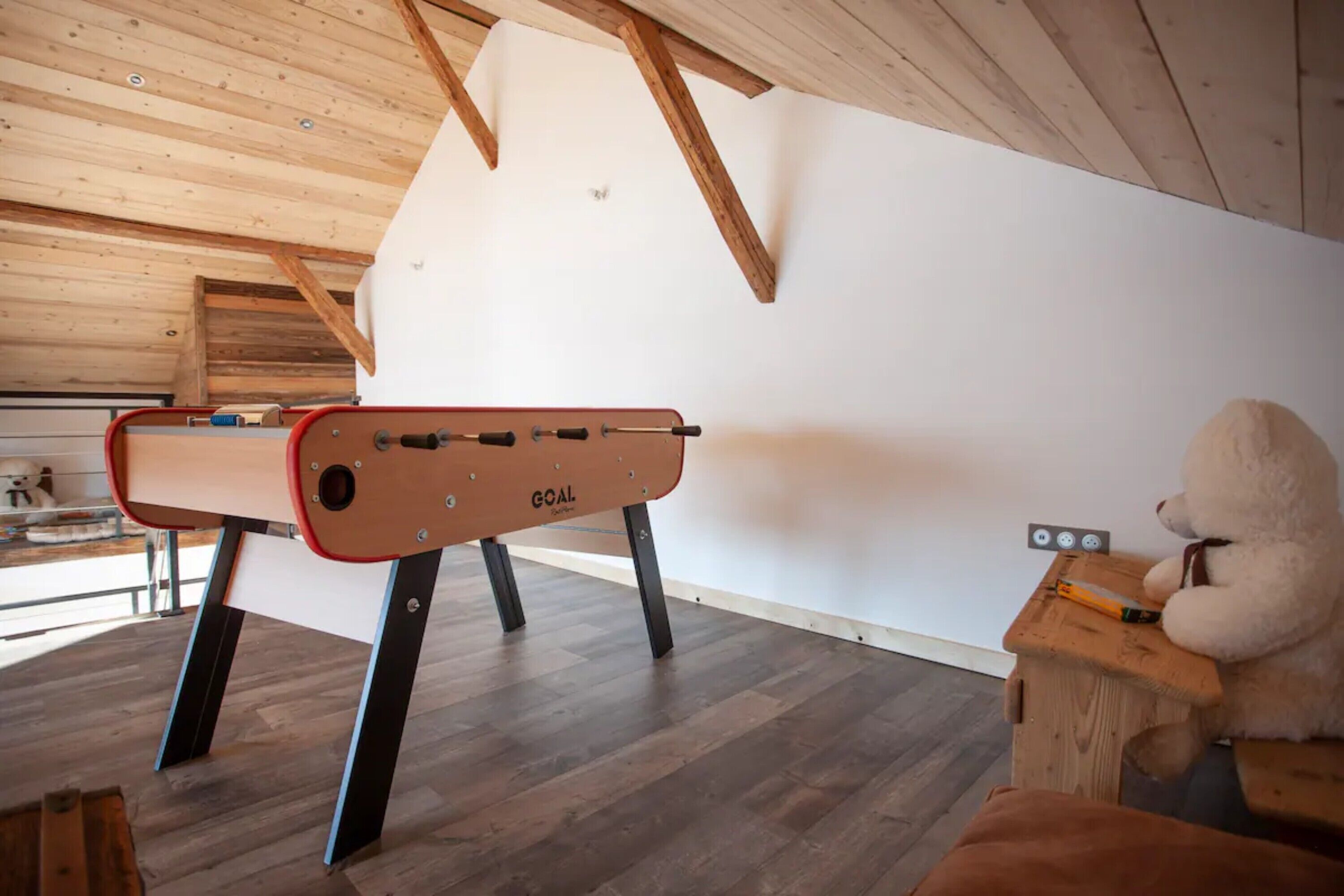 A room with a foosball table, a teddy bear, and a wooden ceiling.